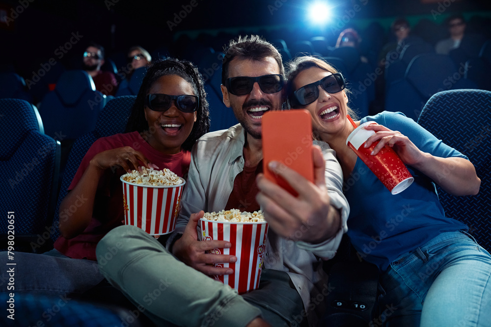 Cheerful friends taking selfie during 3D film projection in movie theater. Cheerful friends taking selfie during 3D film projection in movie theater.