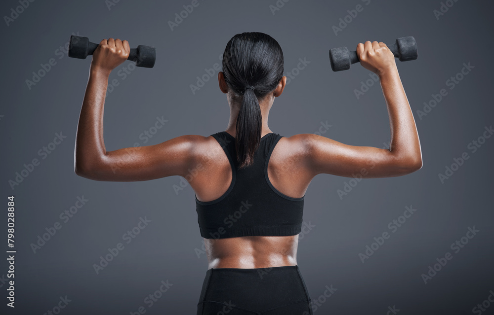Woman, back and dumbbells in studio for arms, athlete for wellness and weight lifting exercise for power. Strong, Indian bodybuilder and health training, muscle and with equipment on background Woman, back and dumbbells in studio for arms, athlete for wellness and weight lifting exercise for power. Strong, Indian bodybuilder and health training, muscle and with equipment on background
