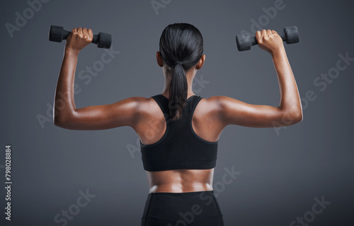 Woman, back and dumbbells in studio for arms, athlete for wellness and weight lifting exercise for power. Strong, Indian bodybuilder and health training, muscle and with equipment on background