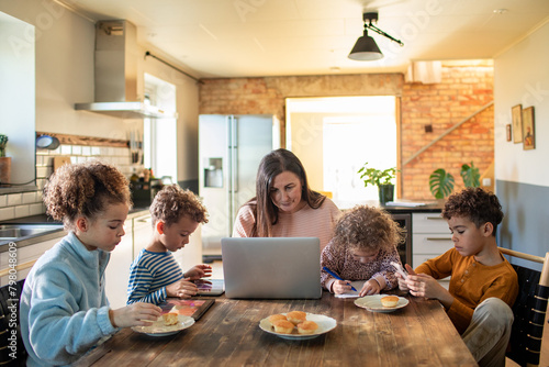Mother multitasking with work and children during breakfast at home photo