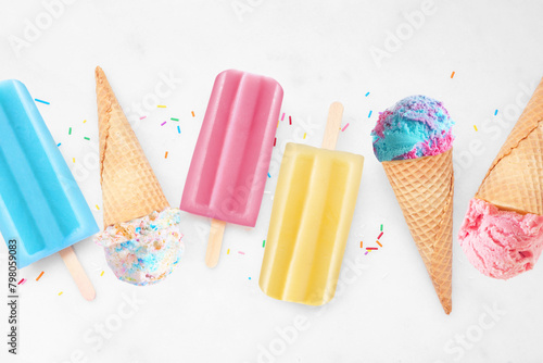Assortment of colorful summer popsicles and ice cream desserts. Above view flat lay on a bright white marble background.