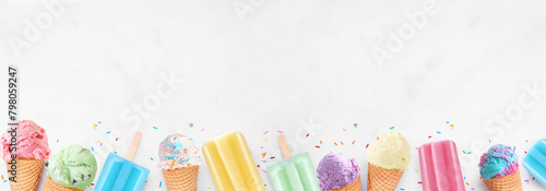 Assortment of colorful pastel ice cream cones and popsicle summer frozen desserts. Top view bottom border on a white marble banner background. Copy space.