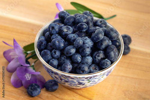 jumbo blueberries overflowing a white dish with blue flowers on a wooden table photo