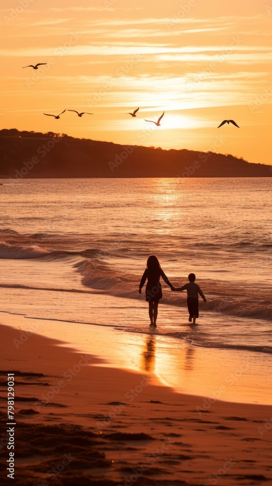 b'Mother and son walking on the beach at sunset'