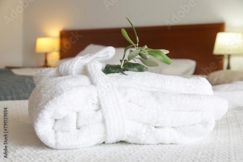 White cotton bathrobe with olive tree twig on the bed in hotel room. Tourism, hotels, hospitality industry