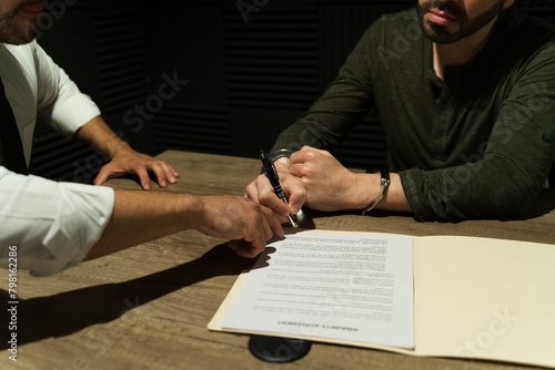 Fotografia Close-up of a suspect signing an immunity deal in the shadows during an interrog