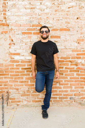 Smiling hispanic man in black t-shirt and jeans posing against a rustic brick wall for a mock-up photo shoot