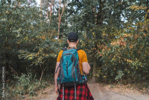 Back view of a young backpacker man walking the forest path