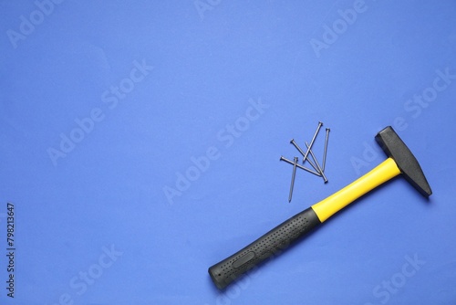 Hammer and metal nails on blue background, top view. Space for text