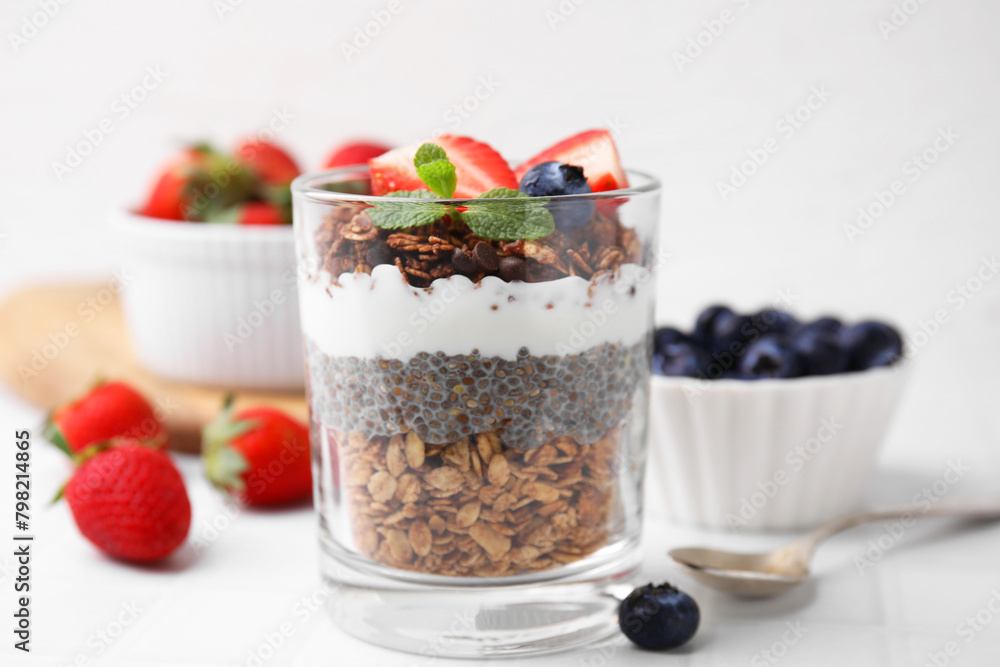 Tasty granola with berries, yogurt and chia seeds in glass on white table Tasty granola with berries, yogurt and chia seeds in glass on white table