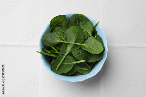 Fresh spinach leaves in bowl on white tiled table  top view