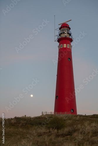 red lighthouse on the coast in the dunes at dusk with full moon rising photo