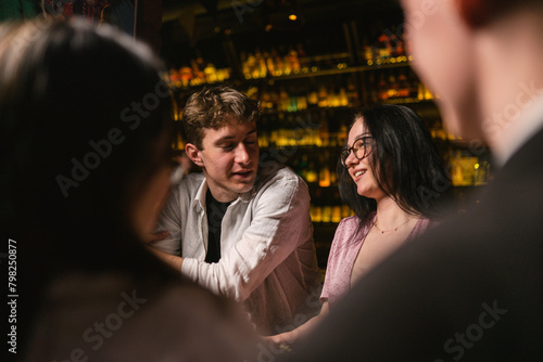 Young people joke and flirt at bar in fancy place with subdued light. Cheerful atmosphere with jokes and various drinks in restaurant