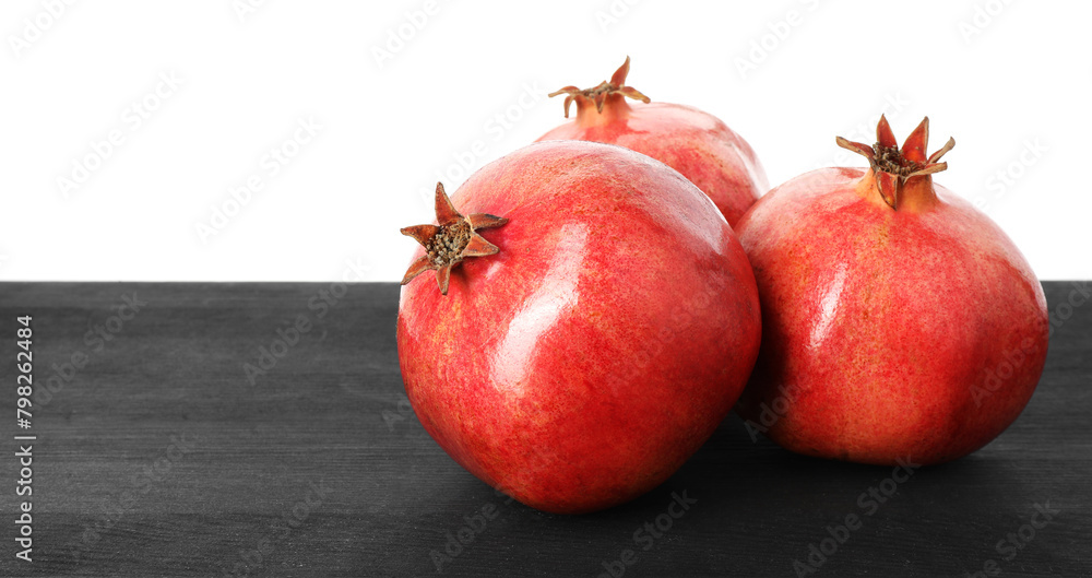 Fresh pomegranates on black wooden table against white background, space for text Fresh pomegranates on black wooden table against white background, space for text