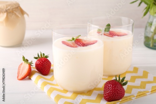 Tasty yogurt and strawberries in glasses on white wooden table, closeup
