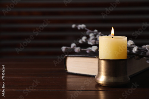 Burning candle  Bible and willow branches on wooden table  closeup. Space for text
