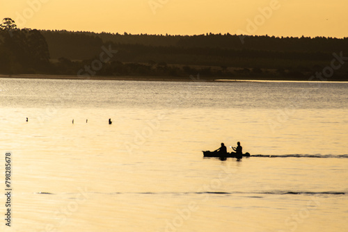 paisaje relajante con siluetas de canoas de pescadores en la hora dorada dejando una estela en el río, Entre Ríos, Argentina 