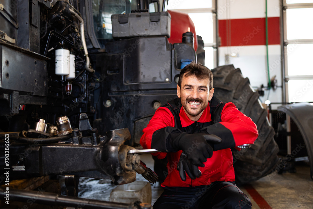 Portrait of experienced mechanic changing wheels on tractor. Service and maintenance of agricultural machinery.