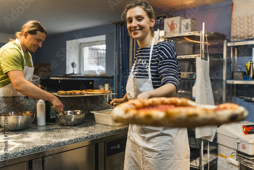 woman cook holding a prepared pizza with a peel and other one working in the background. High quality photo