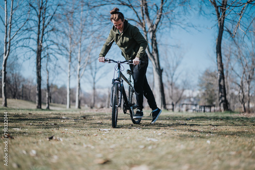 A good looking young man spends his free weekend riding a bicycle outdoors in the park, enjoying a sunny day and the nature around him.