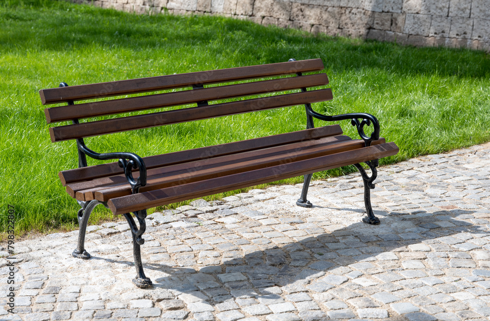 Brown benches for sitting in the city park surrounded by greenery and flowers. Benches for rest and relaxation. Brown benches for sitting in the city park surrounded by greenery and flowers. Benches for rest and relaxation.
