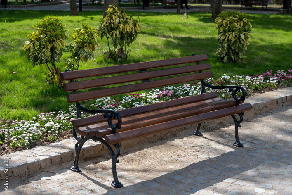Brown benches for sitting in the city park surrounded by greenery and flowers. Benches for rest and relaxation. 
