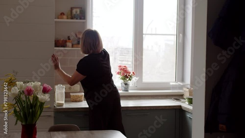Woman tidies up the kitchen and puts everything in its place, cleaning routine photo