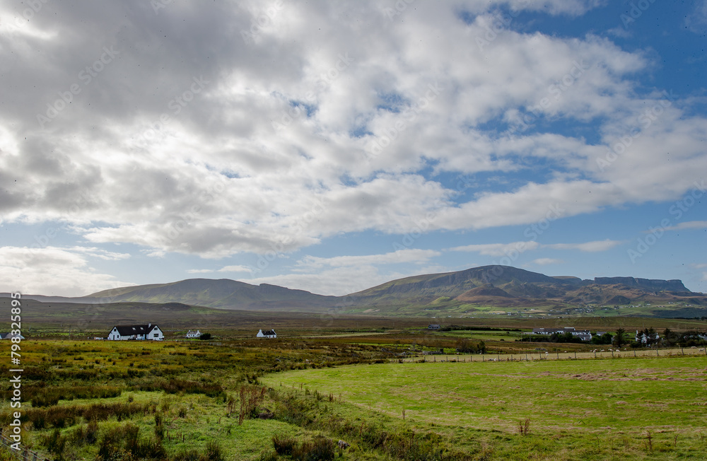 Obraz premium Farm houses on the Scottish hills in the isle of skye. Scotland, with Cuillin Mountains and orange clouds on backround in sunset light, Isle of Skye, Scotland
