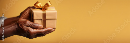 Hands holding a golden gift box with a bow, yellow background, for celebrations and surprises photo
