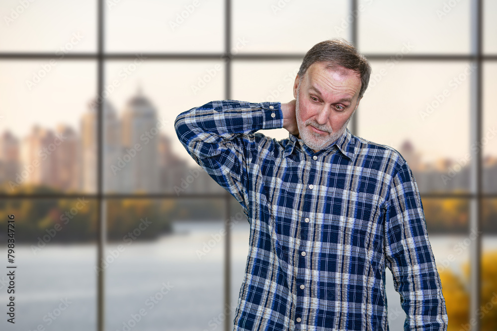 Handsome mature man is touching his neck. Checkered window background. Handsome mature man is touching his neck. Checkered window background.