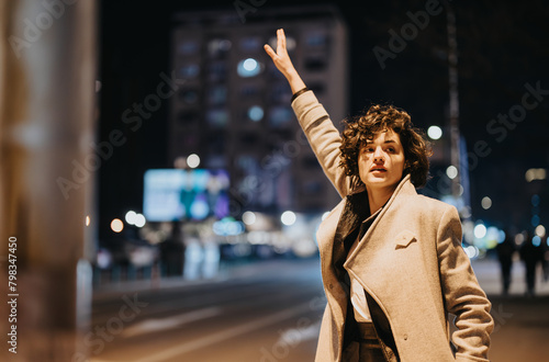 Young woman hailing a cab on a bustling city street at night.