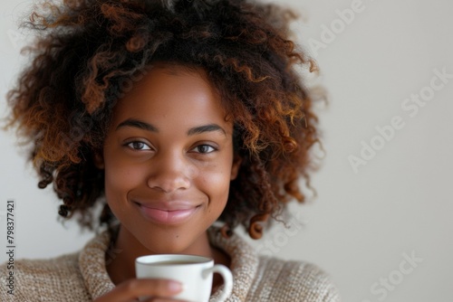 A woman with curly hair is holding a white coffee cup and smiling