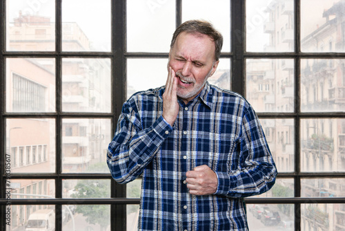 Matureman touching his cheek because of toothache. Checkered windows background. © DenisProduction.com