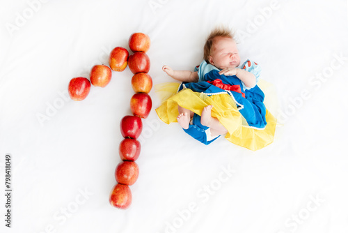 Flat lay picture of a 1 month baby with number made apples. Newborn baby girl in a princess outfit. Fairy tale costume on a baby. 1 month old with a number next to it