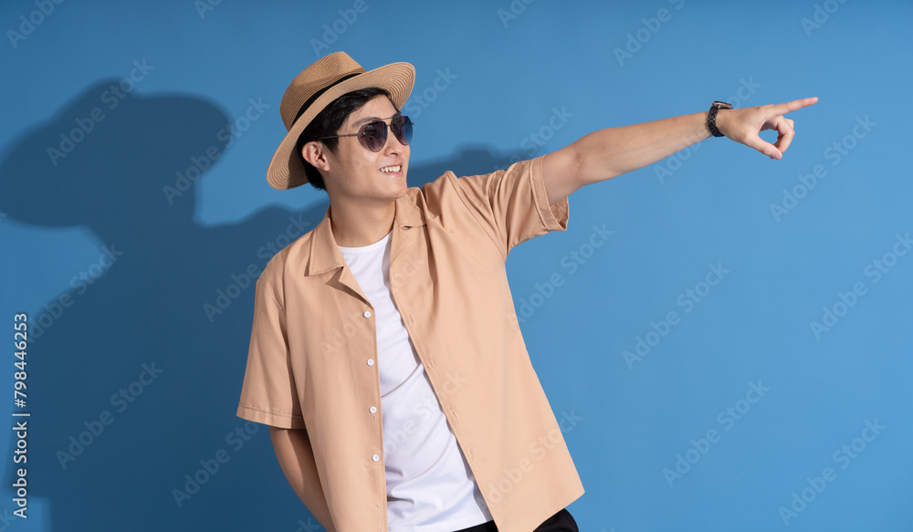 Portrait of Asian man posing on blue background, traveling in summer