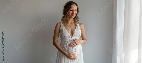 Pregnant caucasian woman in white dress holding hands on belly