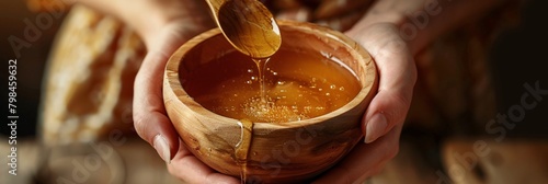 Close-up of female hands delicately holding a wooden bowl filled with golden bee honey and a spoon, amidst the process of crafting organic glycerin-based soap.