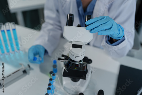 Confident female scientist conducting research in medical laboratory A researcher in the foreground is using a microscope. Medical test tube.