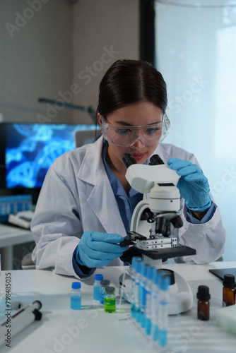 Confident female scientist conducting research in medical laboratory A researcher in the foreground is using a microscope. Medical test tube.