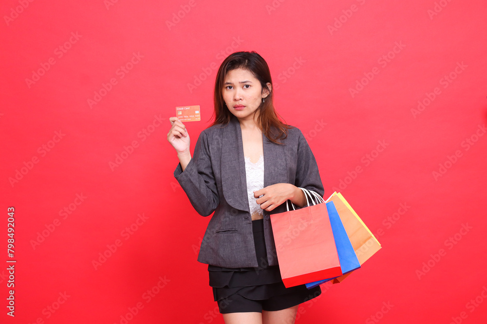 gesture of surprised indonesia office woman at the camera carrying a shopping paper bag and holding a credit debit card wearing a formal suit with a red background. for transaction and business gesture of surprised indonesia office woman at the camera carrying a shopping paper bag and holding a credit debit card wearing a formal suit with a red background. for transaction and business