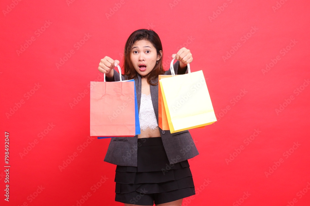 Portrait of a shocked Asian office woman with both hands raising a shopping paper bag in front of her wearing a formal jacket with a red background. for transaction, lifestyle and business concepts Portrait of a shocked Asian office woman with both hands raising a shopping paper bag in front of her wearing a formal jacket with a red background. for transaction, lifestyle and business concepts