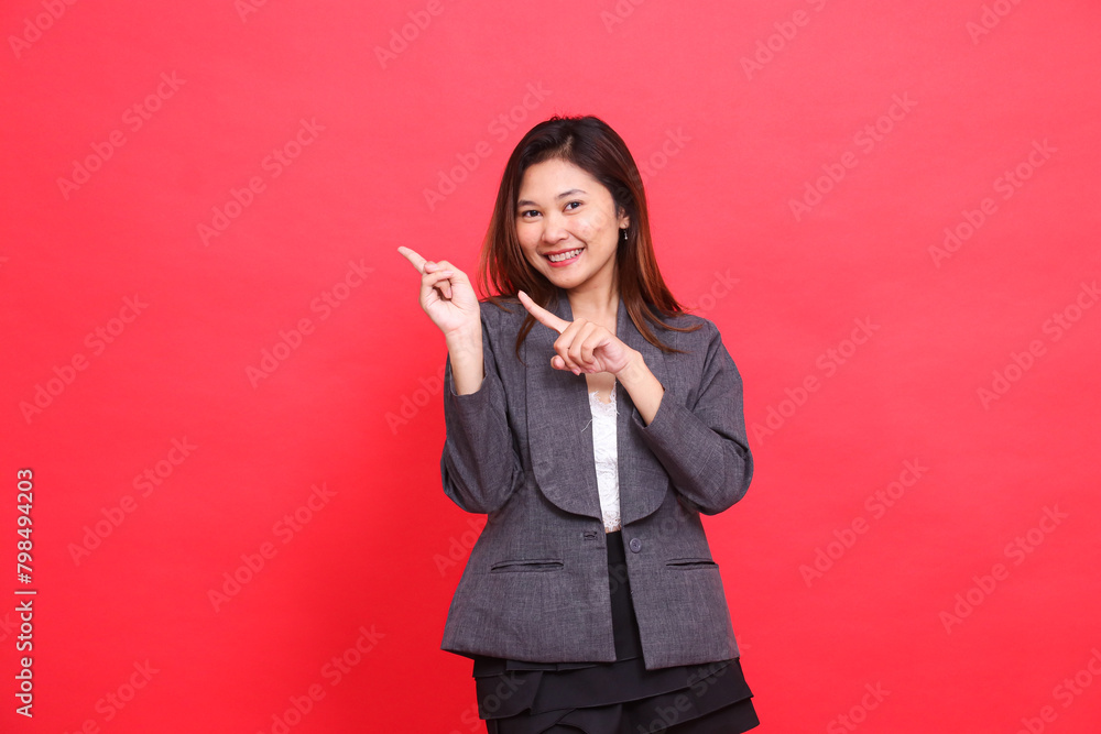 gesture of a cheerful Asian office girl with both hands pointing to the top right, wearing a gray jacket and black mini skirt on a red background. for corporate concepts, publications and advertising