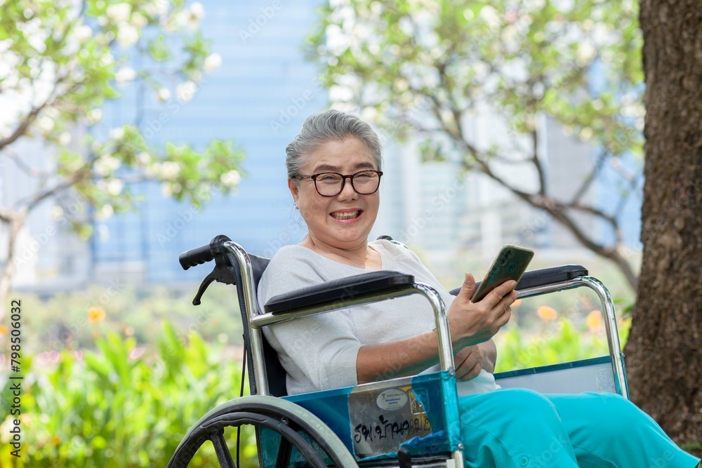 A woman in a wheelchair is smiling and holding a cell phone. Concept of happiness and contentment, as the woman is enjoying her time outdoors A woman in a wheelchair is smiling and holding a cell phone. Concept of happiness and contentment, as the woman is enjoying her time outdoors