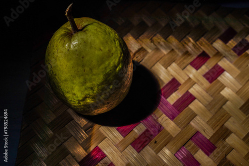 guava fruit isolated on woven bamboo with natural lighting from sunlight, dark background for copy space.