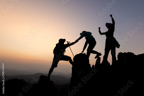 Silhouette of person hikers climbing up mountain cliff and one of them giving helping hand. People success, team work concept.