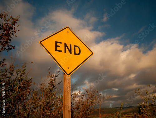 Yellow diamond shaped traffic sign with the word End written on it against a stormy cloudy sky