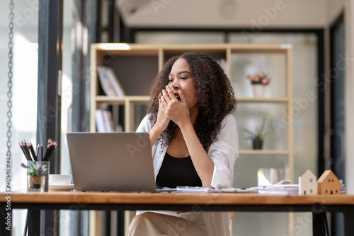 Joyful businesswoman with curly hair celebrating a successful moment while working at her modern office desk.