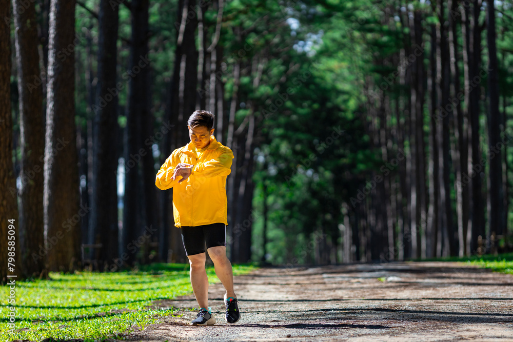 Asian trail runner is running outdoor in pine forest dirt road for exercise and workout activities training while checking smart watch on calories loss achieve healthy lifestyle and fitness concept Asian trail runner is running outdoor in pine forest dirt road for exercise and workout activities training while checking smart watch on calories loss achieve healthy lifestyle and fitness concept