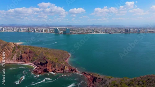 An awe-inspiring drone voyage from a deserted island to Mazatlan's beach, Mexico. Tourist boats leave wakes on the sea, enhancing the view. Nearing the beach, the grandeur of hotels adds prominence. photo
