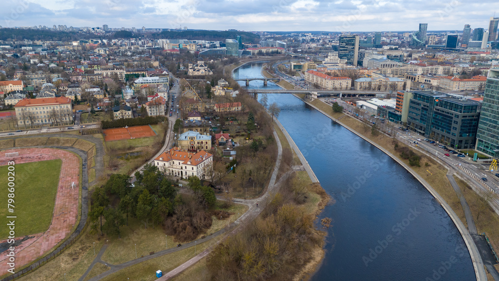 Drone photography of river shoreline going through city and people walking during spring day